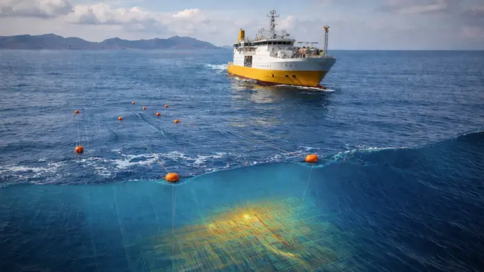 Σεισμικό ερευνητικό πλοίο στη θάλασσα με πλωτήρες και καλώδια μέτρησης, σε φόντο αχνή ακτογραμμή Κρήτης