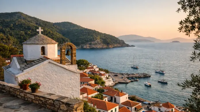 Θέα στη Σκόπελο στο ηλιοβασίλεμα, με ήρεμη θάλασσα, παραδοσιακά σπίτια και εκκλησάκι σε σοβαρό, φυσικό ύφος