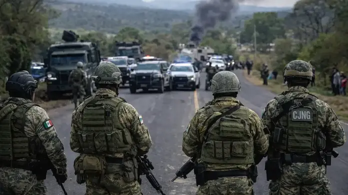 Θεσμική εικόνα από επιχείρηση ασφαλείας σε δρόμο στο Μεξικό, με στρατιωτικά οχήματα και δυνάμεις ασφαλείας σε ανάπτυξη, στο φόντο καπνός και ορεινό τοπίο.