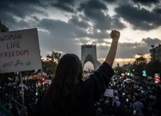 Θεσμική κινηματογραφική εικόνα διαδήλωσης στο Ιράν με σύνθημα Woman Life Freedom και πλήθος πολιτών απέναντι στο καθεστώς