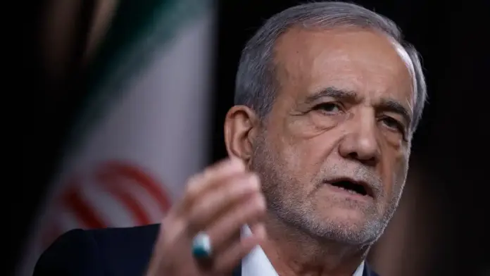 Close-up of Masoud Pezeshkian speaking during a public address with an Iranian flag blurred in the background